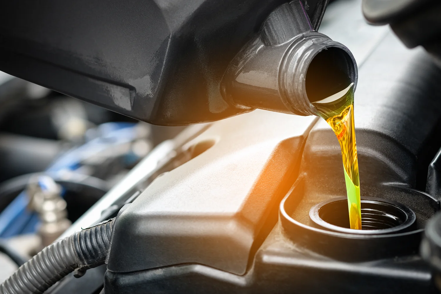 Engine oil being poured from a black container into a car engine during maintenance.
